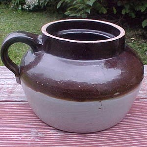 May include: A brown and white glazed stoneware crock with a handle. The crock has a wide mouth and a rounded body.