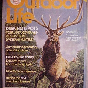 May include: A vintage magazine cover featuring a large, brown elk with antlers, standing in a forest setting. The magazine is titled "Outdoor Life" and the cover text reads "Deer Hotspots, Your Area Coverage - Plus Tips From 5 Veteran Hunters".