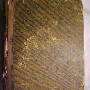 May include: A vintage, brown leather-bound book with a gold-toned, patterned cover. The cover has a faded, worn look, suggesting age and use.