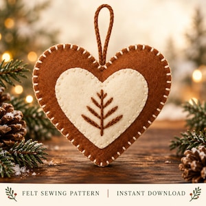 May include: A heart-shaped felt ornament featuring a brown outer layer and a cream-colored inner heart with a brown embroidered tree design. The edges are stitched with cream thread, and a brown cord loop is attached for hanging. Text reads: FELT SEWING PATTERN | INSTANT DOWNLOAD.
