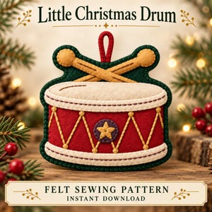 Può includere: Un addobbo natalizio a forma di tamburo in feltro con corpo rosso, cuciture a zigzag gialle, parte superiore bianca e due bacchette beige incrociate. L'ornamento ha un bordo verde scuro e un occhiello rosso. Testo Little Christmas Drum.