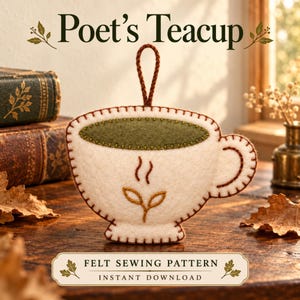 May include: A cream-colored felt teacup ornament featuring a dark green felt interior, brown stitched edges, and a brown hanging loop. The front displays a brown embroidered tea leaf motif with steam lines and the text Poet's Teacup.