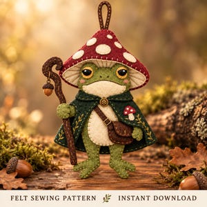 May include: A felt ornament featuring a green frog wearing a red mushroom cap hat and a dark green cape with a brown satchel. The frog holds a brown staff with an acorn charm. The text at the bottom reads FELT SEWING PATTERN INSTANT DOWNLOAD.