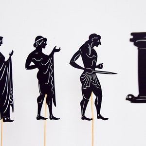 May include: Black paper cutouts of ancient Greek figures and a column on wooden sticks. The figures include a woman in a draped gown, a man with a draped cloth, a man holding a sword, and a classical column.