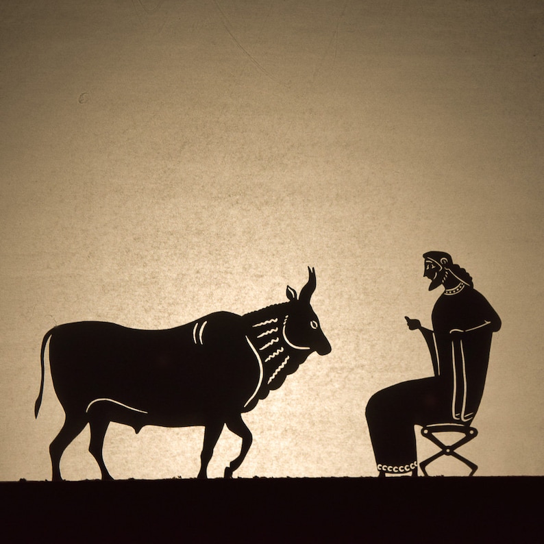 May include: A silhouette illustration depicts a bull facing a seated figure. The bull is black with detailed markings, and the figure is seated on a stool, gesturing with one hand. The background is a light tan color.