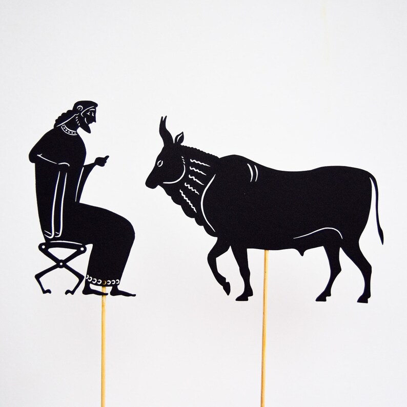 May include: Black silhouette of a seated figure and a bull, both on wooden sticks. The figure is seated on a stool, and the bull is walking. The figures are against a white background. The style is reminiscent of ancient Greek art.