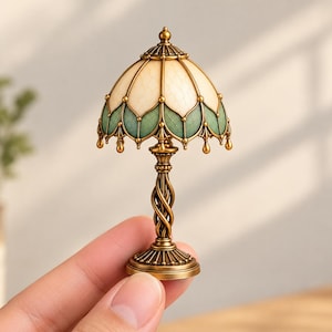 May include: A miniature table lamp featuring a dome-shaped shade with cream and sage green panels, accented by a metallic bronze finish. The lamp has a twisted central column and a circular base, showcasing intricate detailing throughout.