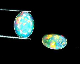 May include: Two oval-shaped opals with a translucent, milky white base and vibrant flashes of red, orange, green, and blue color play. One opal is held by metal tweezers, while the other rests nearby, both displaying a faceted surface finish.