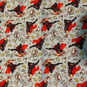May include: Light blue fabric featuring a repeating pattern of the superhero Thor in action poses. The design includes Thor with his hammer, lightning bolts, stars, and the word "THOR" in a speech bubble.
