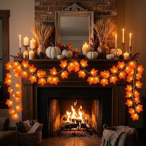 May include: A string of illuminated artificial maple leaves in vibrant orange and yellow hues draped across a fireplace mantel. The garland features warm glowing lights integrated among the foliage, creating a bright, festive display.