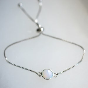 May include: A silver chain bracelet with a white opal gemstone. The bracelet has an adjustable sliding clasp.