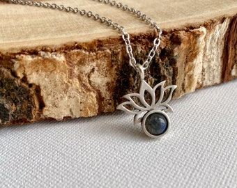 May include: A silver necklace with a lotus flower pendant featuring a dark blue gemstone.