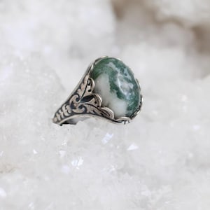 May include: A silver ring with an ornate design and a green and white agate stone.