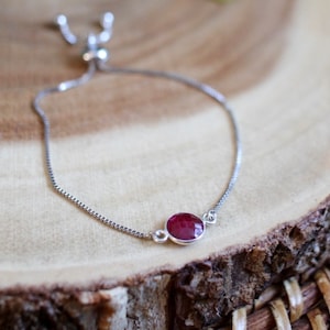 May include: A silver chain bracelet with a red gemstone pendant. The bracelet has an adjustable sliding clasp.
