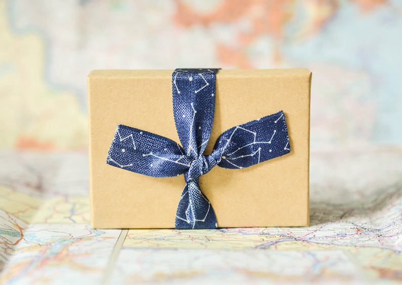 Puede incluir: Una peque&ntilde;a caja de regalo marr&oacute;n atada con una cinta azul con un patr&oacute;n de constelaci&oacute;n blanca.