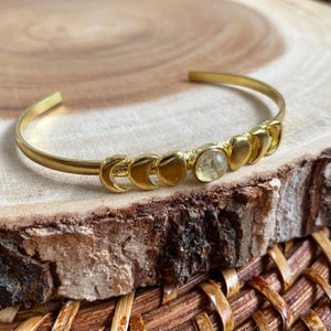 May include: Gold bracelet with a crescent moon design and a clear gemstone in the center.