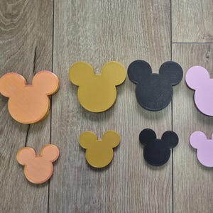 May include: A collection of ten flat, mouse-shaped icons arranged in two rows. The top row features five larger icons in orange, gold, black, light pink, and white. The bottom row contains five smaller matching icons in the same five colours.