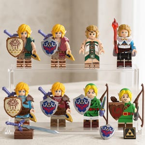 May include: A collection of eight plastic minifigures inspired by video game characters, featuring various outfits, shields, and swords. The figures are displayed on a two-tiered clear acrylic stand, with additional accessories like a sword and shield placed on the base.