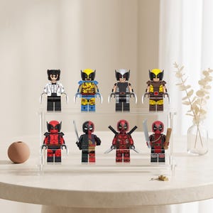 May include: A collection of eight plastic minifigures arranged on a two-tiered clear acrylic display stand. The top row features four characters with claw accessories, while the bottom row includes four characters equipped with various swords and bat weapons.