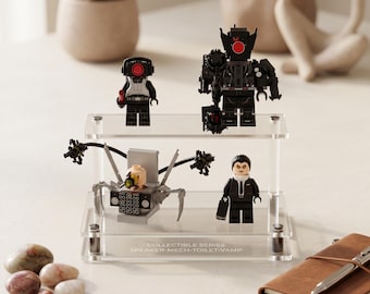 May include: A two-tiered clear acrylic display stand holding four small plastic figures. The base features the text COLLECTIBLE SERIES SPEAKER-MECH-TOILET-VAMP. The figures include a black robot, a small black character, a grey mechanical unit, and a vampire.