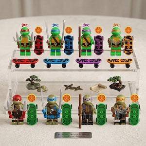 Può includere: Una collezione di otto minifigure delle Tartarughe Ninja esposte su un supporto trasparente a più livelli. Il set include accessori come skateboard, armi, gettoni pizza e alberi bonsai. Una targhetta metallica riporta la scritta Heroic Ninja Squad.