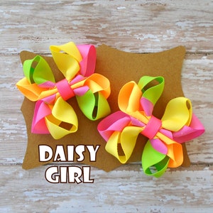 May include: Two yellow, pink, and green ribbon bows on a brown card with the text "Daisy Girl".