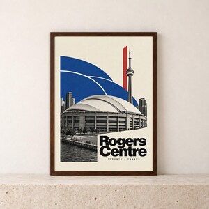 May include: A framed art print featuring a black and white photograph of the Rogers Centre stadium and the CN Tower in Toronto, Canada. The design includes bold blue curved shapes and a vertical red rectangle against a cream background.