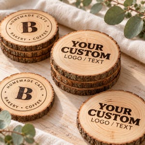 Könnte beinhalten: Ein Set aus runden Holzuntersetzern mit natürlicher Rindenkante. Einige Untersetzer zeigen ein kreisförmiges Logo mit dem Buchstaben B und dem Text HOMEMADE CAFE BAKERY COFFEE, andere tragen den Text YOUR CUSTOM LOGO / TEXT in schwarzer Schrift.