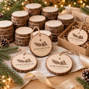 Könnte beinhalten: Eine Sammlung runder Holzanhänger mit natürlicher Rindenkante, die ein lasergraviertes Design aus einem Kiefernzweig, einem Stern und dem Text NORTHWOOD STUDIO zeigen. Jeder Anhänger verfügt über eine Juteschnur zum Aufhängen.