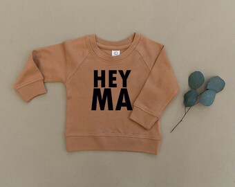 May include: A brown long-sleeve sweatshirt with the text "HEY MA" printed in black on the front.