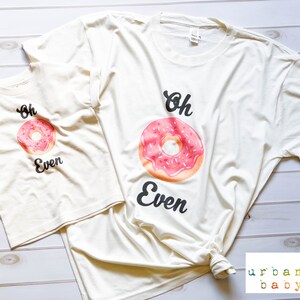 May include: Two cream colored t-shirts with a pink and white donut graphic and the text "Oh Even".