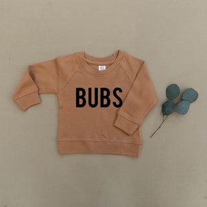 May include: A brown long-sleeved sweatshirt with the word "BUBS" printed in black on the front.