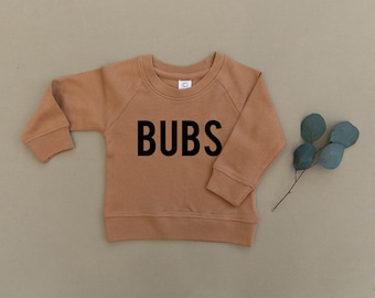 May include: A brown long-sleeved sweatshirt with the word "BUBS" printed in black on the front.