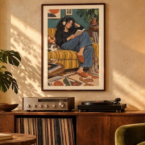 May include: A framed wall art print depicting a person with curly dark hair wearing headphones and reading a book while sitting on a striped yellow sofa. The illustration includes a cat, a houseplant, a record player, and vinyl records in a room.