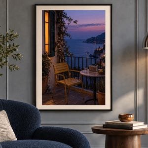 May include: A framed wall art print depicting a balcony scene at dusk, featuring a yellow chair and a small round table overlooking a coastal landscape with a dark blue sea, a purple sunset sky, and a warm glowing window light on the left side.