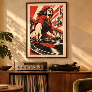 May include: A framed wall art print featuring a stylized illustration of a person wearing headphones and operating a turntable. The artwork uses a bold color palette of red, black, and white, depicting a dynamic scene with sunburst lines.