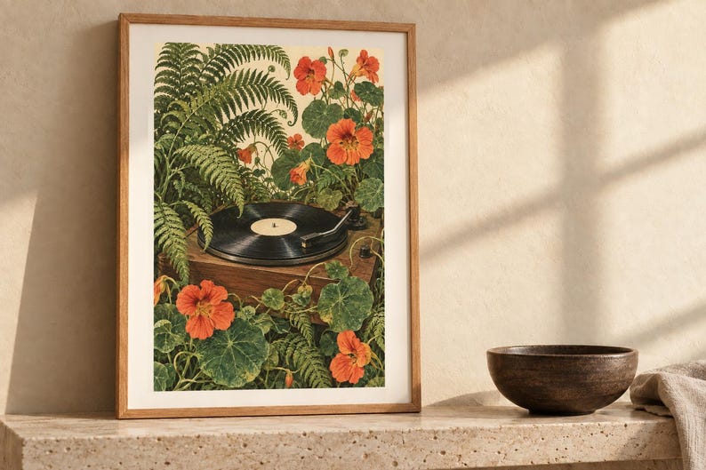 Puede incluir: Una l&aacute;mina de arte enmarcada que muestra un tocadiscos de vinilo negro rodeado de frondosos helechos verdes y flores de capuchina de color naranja vibrante. La ilustraci&oacute;n representa un tocadiscos de madera entre un denso follaje bot&aacute;nico.
