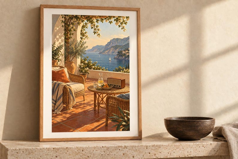 May include: A framed wall art print depicting a Mediterranean terrace with wicker furniture, a radio, and a glass carafe on a round table, overlooking a blue sea with mountains and sailboats under a clear sky with climbing vines.
