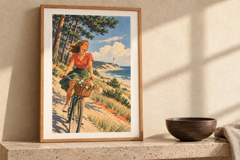 May include: A framed art print featuring a person riding a bicycle with a basket of flowers along a sandy coastal path. The scene includes pine trees, a distant lighthouse, and a blue ocean under a bright sky with white clouds.