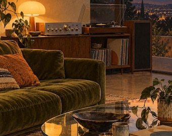 Puede incluir: Una sala de estar con un sofá de terciopelo verde oscuro, una mesa de centro de cristal con cuencos de cerámica y un mueble multimedia de madera con tocadiscos, amplificador y discos de vinilo, frente a una vista del atardecer.