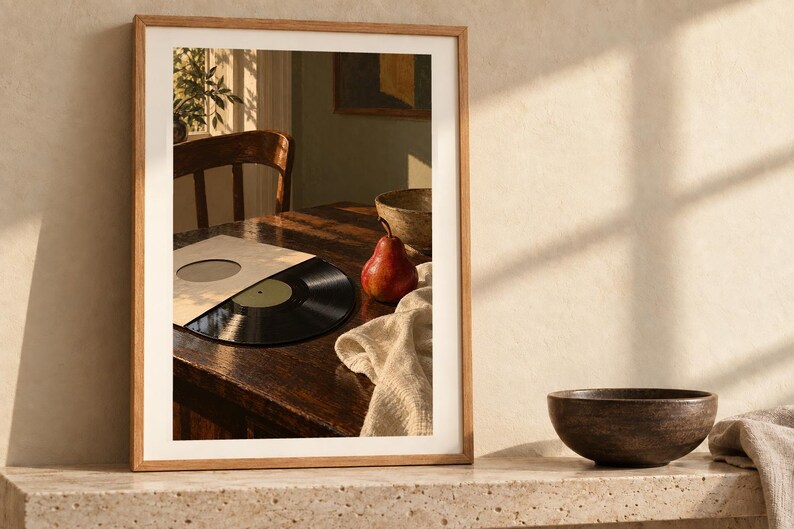May include: A framed wall art print featuring a photograph of a dark wooden table with a black vinyl record in a sleeve, a red pear, a textured cloth, and a wooden bowl, all illuminated by warm sunlight casting long shadows across the scene.