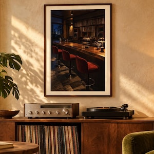 May include: A framed wall art print depicting a dimly lit bar interior with a long wooden counter and several red upholstered bar stools. The artwork is displayed in a room featuring a wooden media console, a turntable, a receiver, and a green plant.