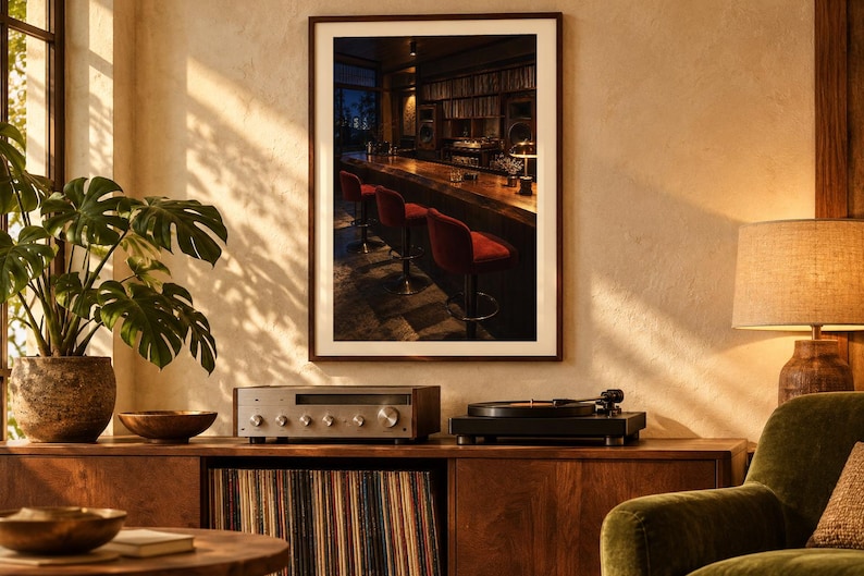 May include: A framed wall art print depicting a dimly lit bar interior with a long wooden counter and several red upholstered bar stools. The artwork is displayed in a room featuring a wooden media console, a turntable, a receiver, and a green plant.