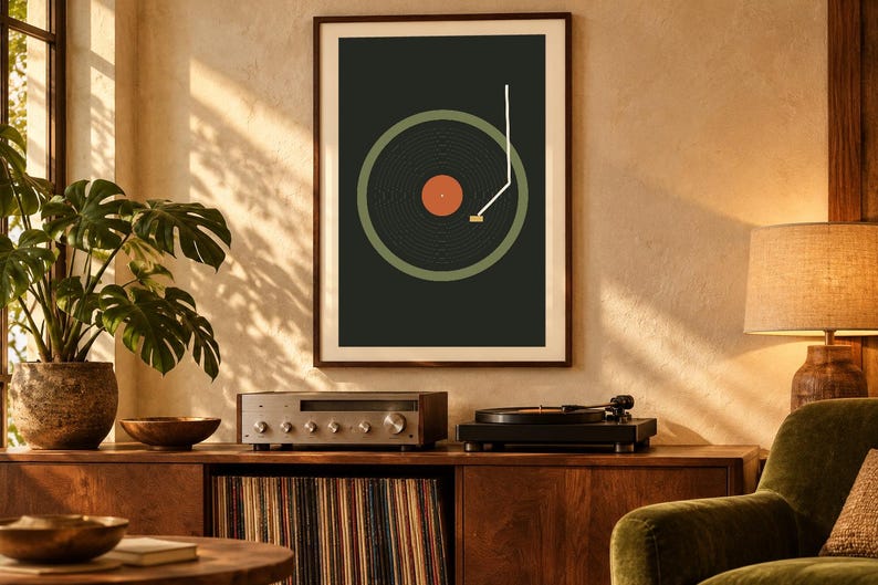 May include: A framed wall art print featuring a graphic illustration of a vinyl record player. The design displays a dark gray background, a muted green circular record, a central orange label, and a white tone arm line.