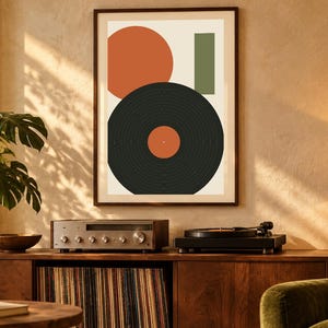 May include: A framed wall art print featuring a large orange circle, a vertical green rectangle, and a black vinyl record graphic with an orange center label, all arranged on a light cream background within a dark brown frame.