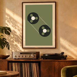 May include: A framed wall art print featuring a sage green background with a graphic illustration of two black circular tape reels connected by thin white lines, each reel containing three small circles in white and green.
