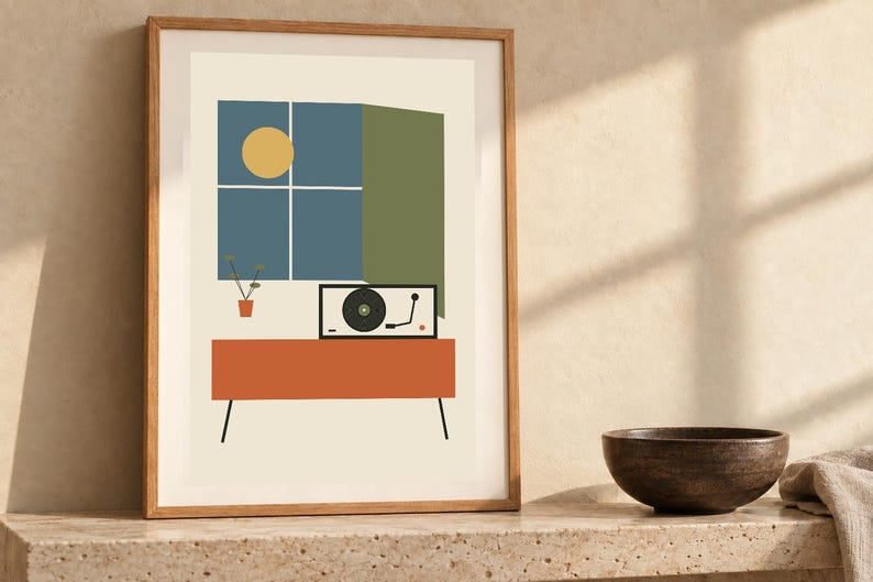 May include: A framed wall art print featuring a graphic illustration of a record player on an orange console table. Above the table is a blue window with a yellow sun and a small potted plant. The print is set against a cream background.