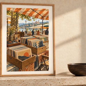 May include: A framed art print depicting an outdoor market scene with wooden crates filled with vinyl records. The scene features orange and white striped awnings, people walking near a waterfront, and a distant town under a bright sky.