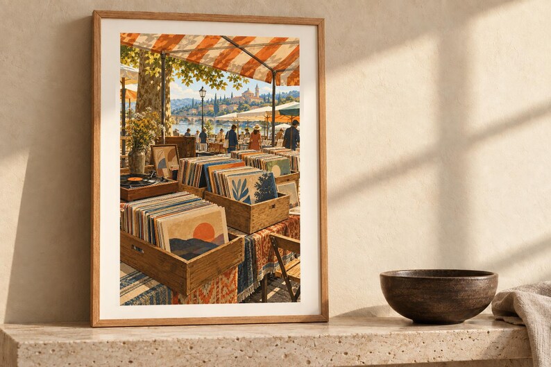 May include: A framed art print depicting an outdoor market scene with wooden crates filled with vinyl records. The scene features orange and white striped awnings, people walking near a waterfront, and a distant town under a bright sky.
