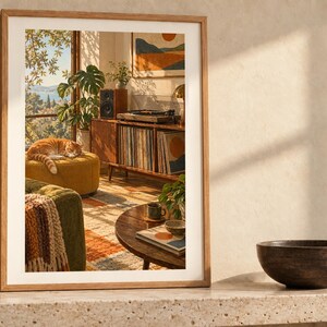 May include: A rectangular wooden frame containing a print of a sunlit living room scene featuring a sleeping orange tabby cat on a yellow ottoman, a record player on a wooden console, a green sofa, and a round coffee table.